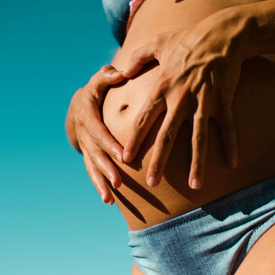 Hands resting on a pregnant belly in the shape of a heart