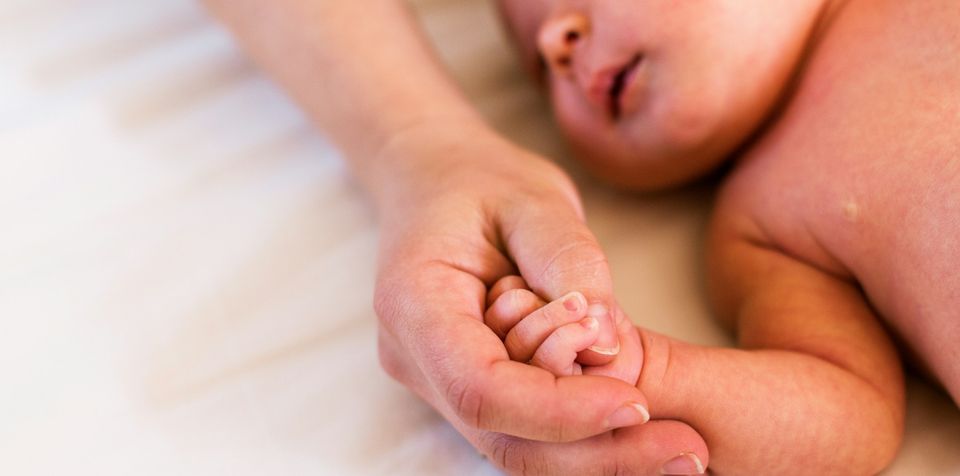 A parent's hand holding their newborn's hand